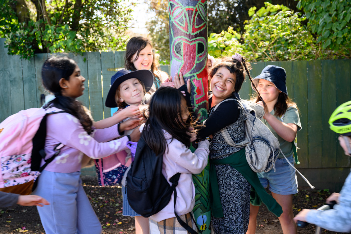 A group of schoolchildren embrace one of the pou