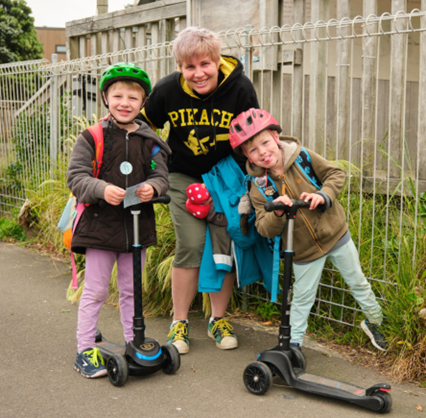 An adult and two children with scooters smile at the camera